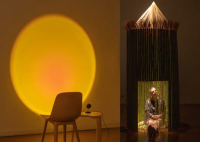 2 photos of one a dimly lit photo of a chair and a stool with a sunset light on the stool (projected onto a wall) in front of the chair. The second photo a women sitting inside a round bamboo structure with a yellow wool door you can partially see through. The art installation is set up in a studio space at night with just one spotlight above lighting the structure.