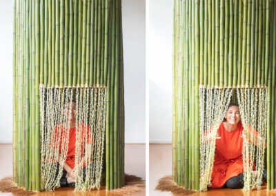women in an orange dress sitting inside a round bamboo structure with a yellow wool door you can partially see through