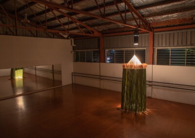 shot of a large dance studio at night and inside a round bamboo structure with a pointed roof constructed from wool. The piece is an immersive art installation and relies on one warm spotlight to dimly lit the structure and space.