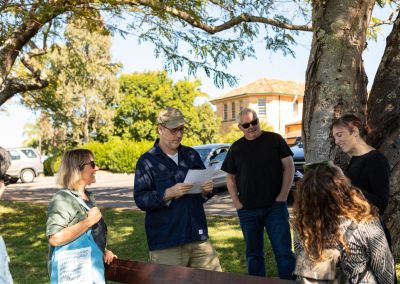 people underneath a tree listening to two indviduals read a script