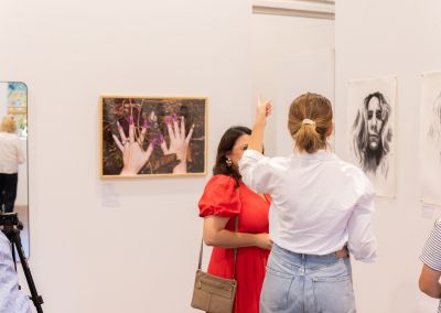 a photo taken from a gallery opening, in the photo are two women chatting and behind them is art on the walls
