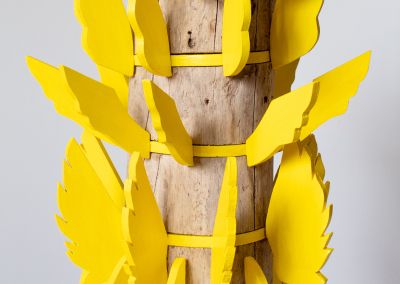 middle half of a sculpture made of a found wooden stump and then layers of bright yellow ply. Those layers have bright yellow ply wings extended outwards