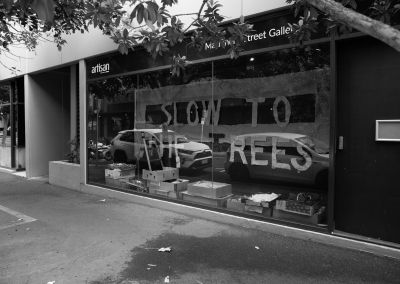 a b&w photo of artisan's machinery street window gallery in Brisbane/meanjin. It shows the install of slow to the trees which is a text based artwork. The window is filled with the mockup paper sheet which says "slow to the trees"