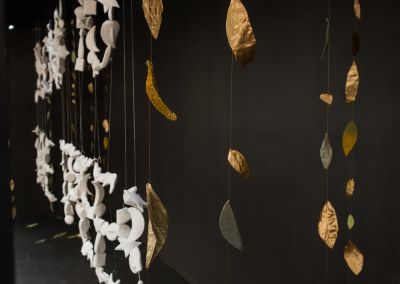 close up shot of a window gallery installation it shows fabric gold leaves hanging against a charcoal painted background and hanging ceramic pieces