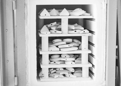 a b&w photo taken inside an open kiln door, it shows 4 stacked shelves of porcelain shapes