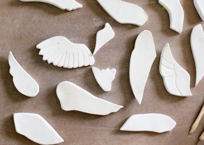 an above shot taken of unfired white porcelain wings of different shapes on a brown board